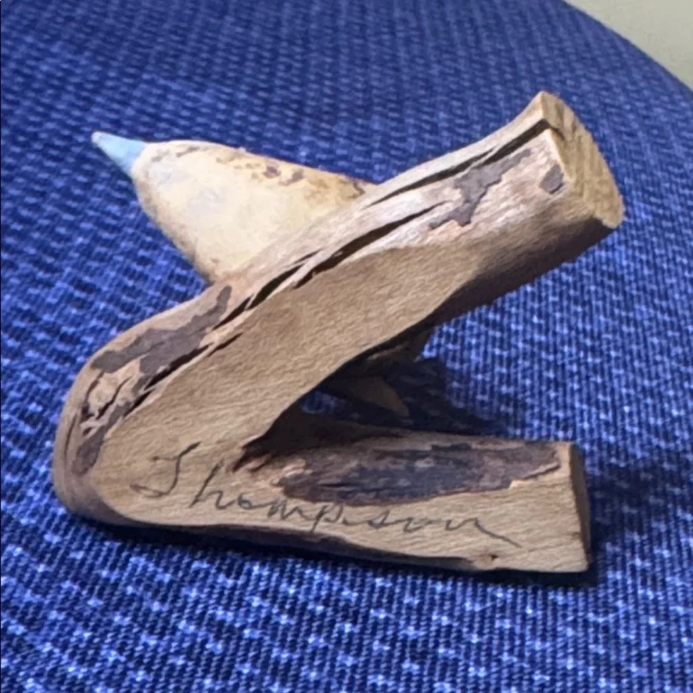 Hand carved wooden bird sculpture perched on a piece of natural wood signed